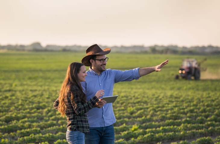 25+ Key Family Farm Statistics 1 Two farmers man and woman with tablet standing in soybean field in front of tractor at sunset