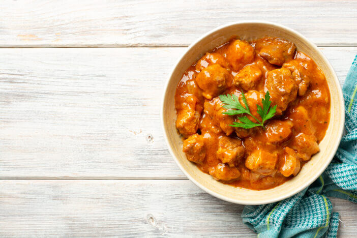 Meat stew in bowl on rustic wooden background. Top view, copy space.