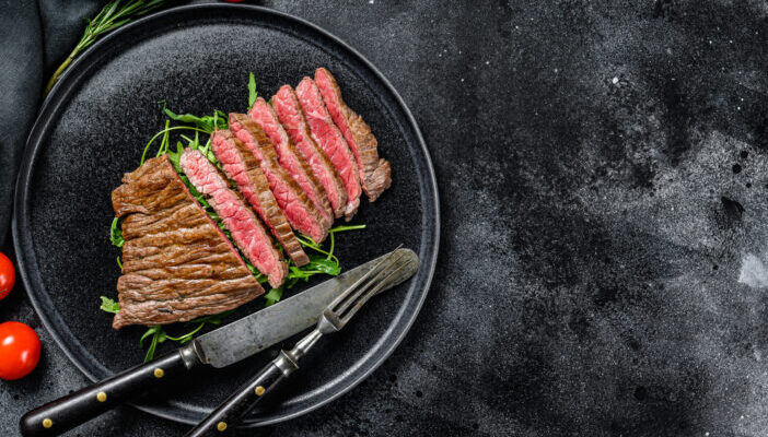 Grilled and cut Flat Iron steak. Marble beef meat. Black background. Top view. Copy space.