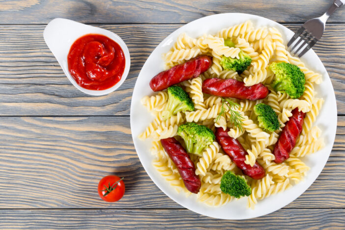 Pasta salad with broccoli and grilled sausages, top view