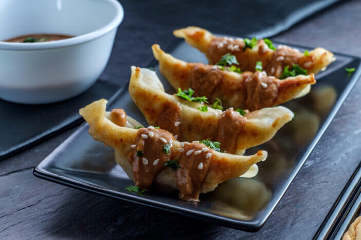 Fried Chinese Hunan pork dumplings with spicy peanut butter sauce and sesame seeds