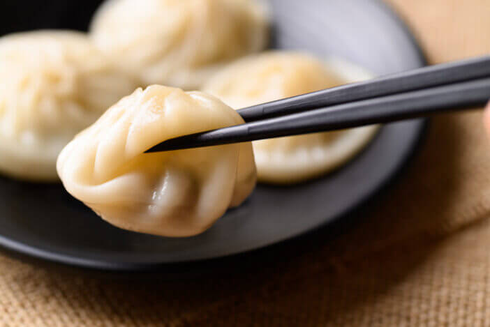 Xiao long bao, small Chinese steamed bun filling with minced pork on black plate eating by use chopsticks