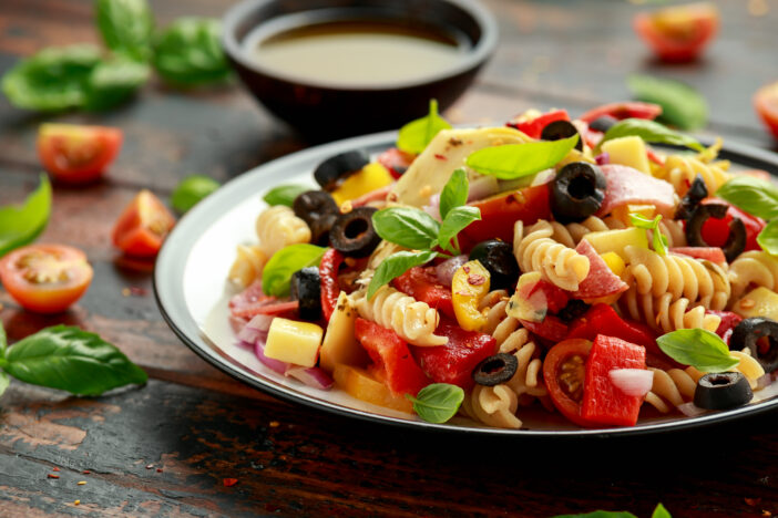 Antipasto salad with pasta, tomato, olives, red onion, bell pepper, salami, cheese, artichoke and basil.