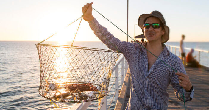 young happy and proud attractive fisherman showing fish and crabs basket net captures smiling at sea dock sunset in man fishing as weekend hobby concept and holidays leisure concept