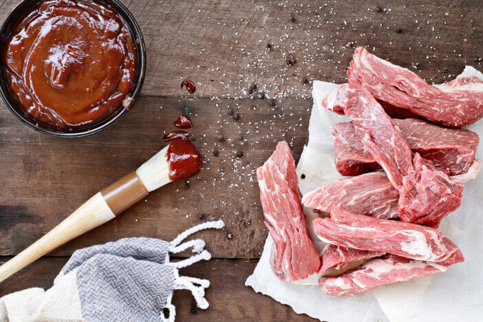 Country ribs with barbecue sauce and basting brush over a rustic table.