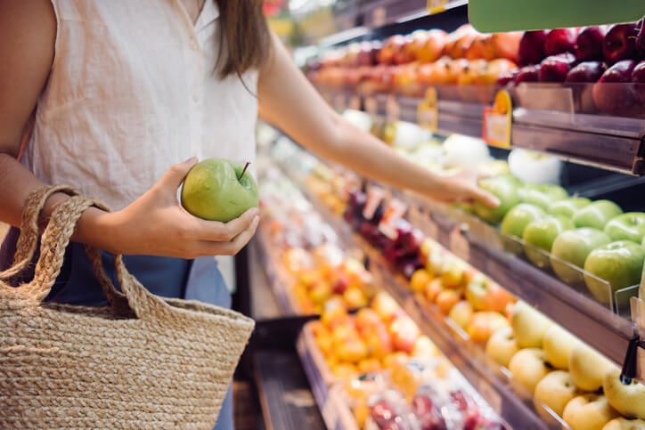 26+ Curious Organic Food Consumption Statistics 1 a woman holding a green apple for shopping in a grocery store, vegan lifestyle concept.