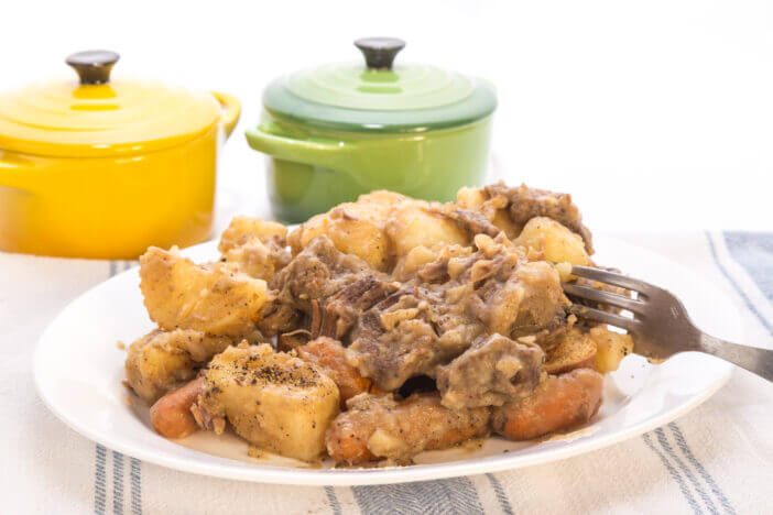 Plate of venison stew on old kitchen dish cloth with white background.