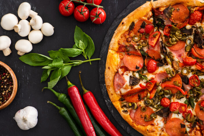 top view of delicious Italian pizza with vegetables and salami on black background