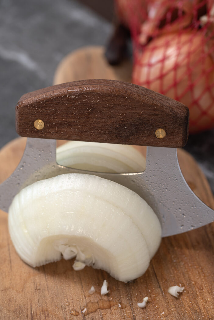 5+ Reasons Why an Alaska Skinning Knife is the Perfect Outdoor Tool 2 Slicing an onion on wooden cutting board with an Alaskan ulu knife.