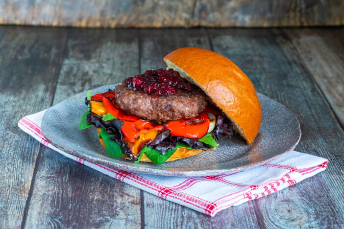 Venison burger in brioche bun with peppery leaf salad, onion, roast peppers and lingonberry sauce