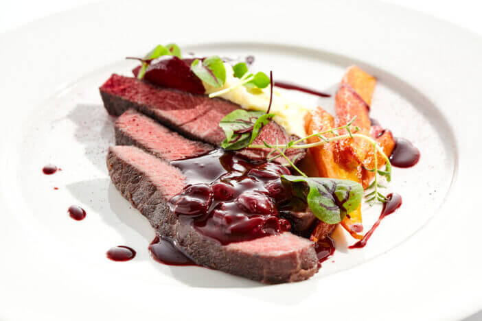 Venison steak with baked vegetables isolated on white plate. Meat steak medium rare roasted with carrot, beetroot and mashed potatoes with cherry sauce. Wild meat in restaurant menu