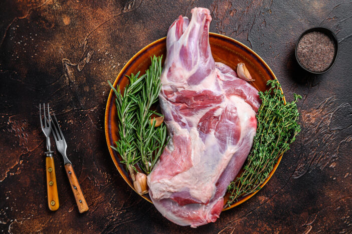 Whole fresh Raw lamb shoulder meat on a plate. Dark wooden background. Top view.