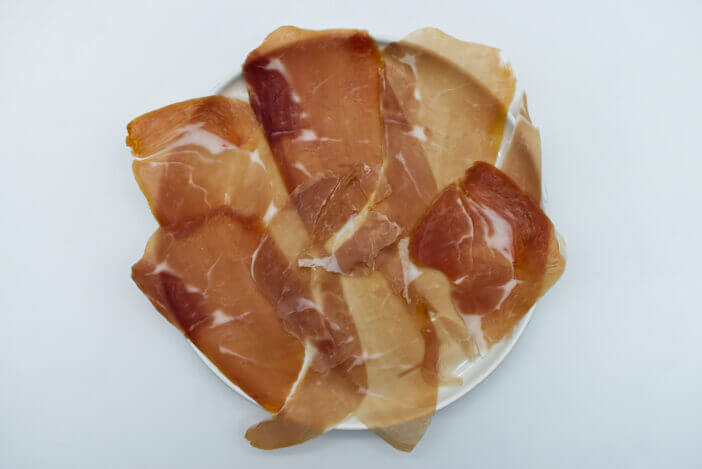 Slices of Italian prosciutto di parma, Italian ham, in a white dish isolated on white. Top view