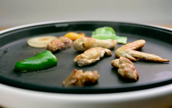 Grill chicken wings and thighs with vegetables on a hot plate. An image of a dinner menu that you can enjoy with your family around the iron plate.