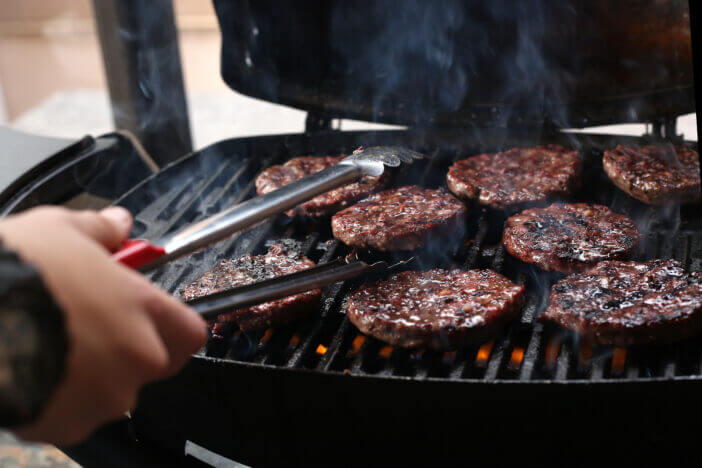 A General view of burger patties being turned on a gas grill