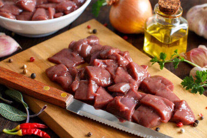 Raw beef liver with spices, herbs and vegetables on a wooden table