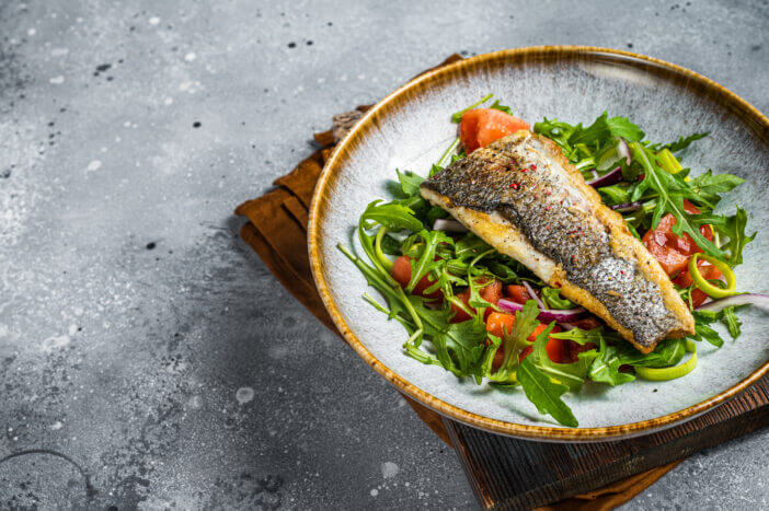 Fried sea bass fillet with vegetable salad, Dicentrarchus fish. Gray background. Top view. Copy space.