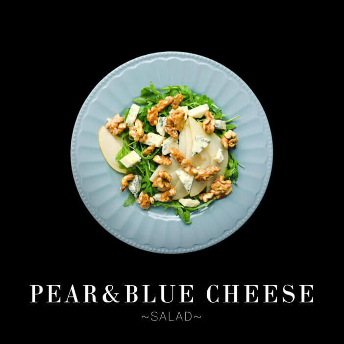 Classic French salad with fresh Pear, blue cheese, fresh arugula, and honey caramelized walnuts served on blue plate. Dish isolated on black background. Text space web banner
