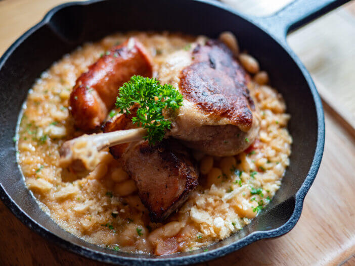 10+ Delicious Ways to Cook with Pork Fatback 3 Sizzling hot, rich, slow-cooked Trio Cassoulet of duck confit, pork belly and smoked sausage on a bed of white beans in a black cast iron pan on a wooden table. Natural Light.