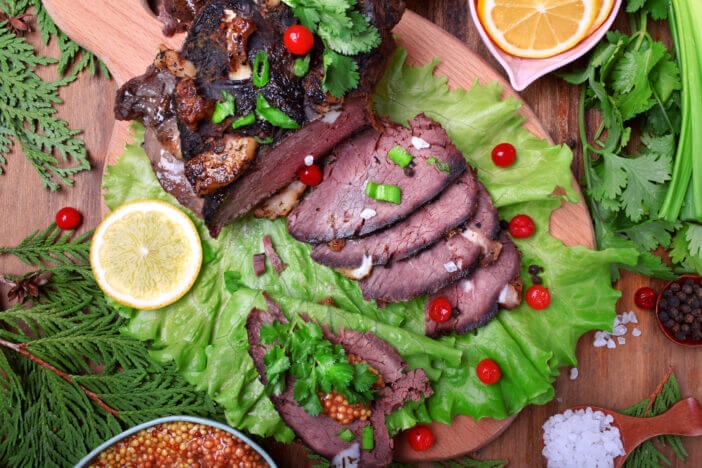 Baked elk ham sliced and topped with greenery and cranberries on the salad leaves. Served meat meal