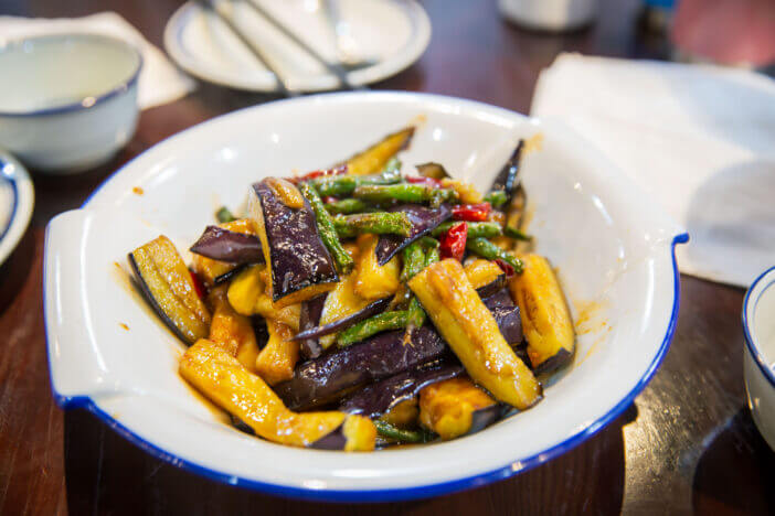 Braised eggplant slices in bean sauce of traditional Chinese Hunan spicy cuisine Asian gourmet meal food dish on the brown wooden table, to share with people eating with chopsticks and plates bowls