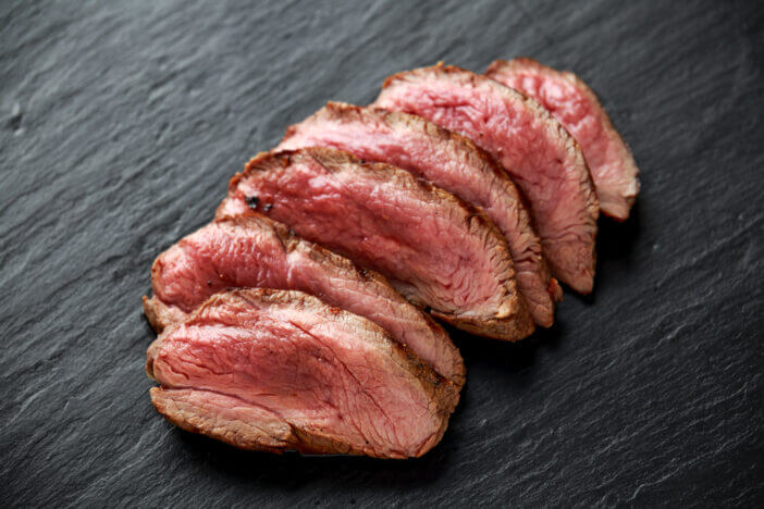 Medium rare venison steak on rustic dark stone board.