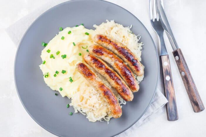 Roasted nuremberg sausages served with sour cabbage and mashed potatoes, on a gray plate, horizontal, top view