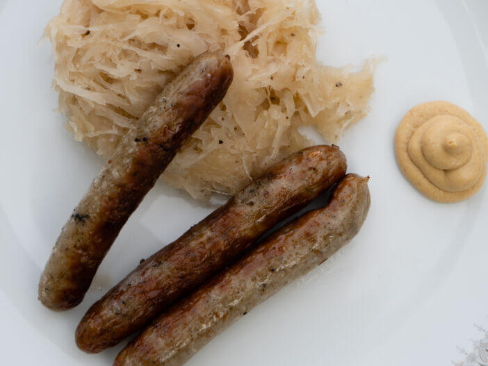 Nuremberg Grilled Sausage or Nürnberger Rostbratwurst with Sauerkraut or Sour Cabbage and Mustard on a White Plate Close Up