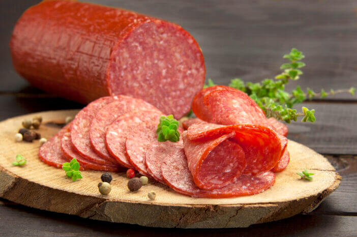 halved in slices turkey salami served on a slice of wood with thyme and ground pepper