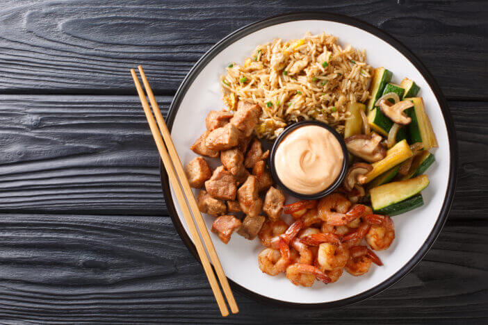 Serving hibachi of rice, shrimp, steak and vegetables served with sauce closeup in a plate on the table. Horizontal top view from above