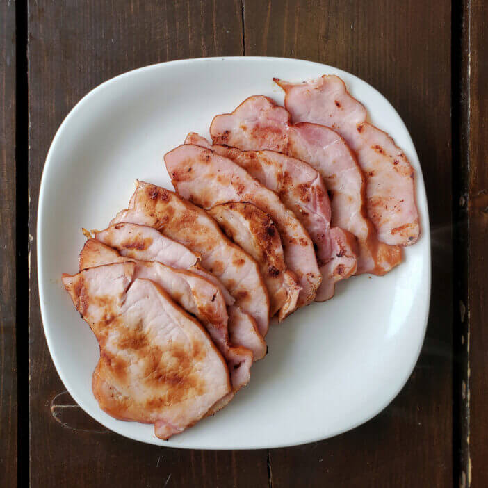 slices of Canadian back bacon in a pile on a white plate