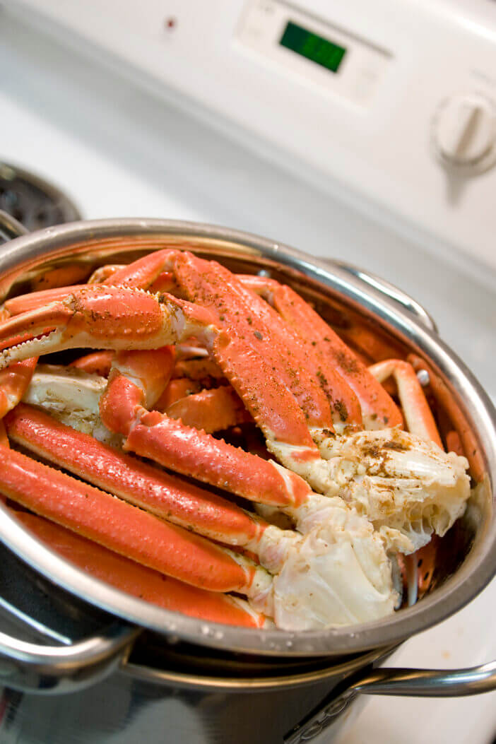 Shallow DOF view of crab legs being steamed on a home stovetop.