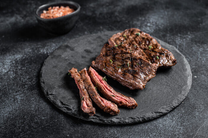 Traditional barbecue skirt steak sliced on a cutting board. Black background. Top view.