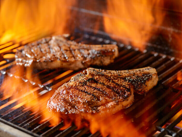 two rib-eye steaks grilling on the open flame with grill marks