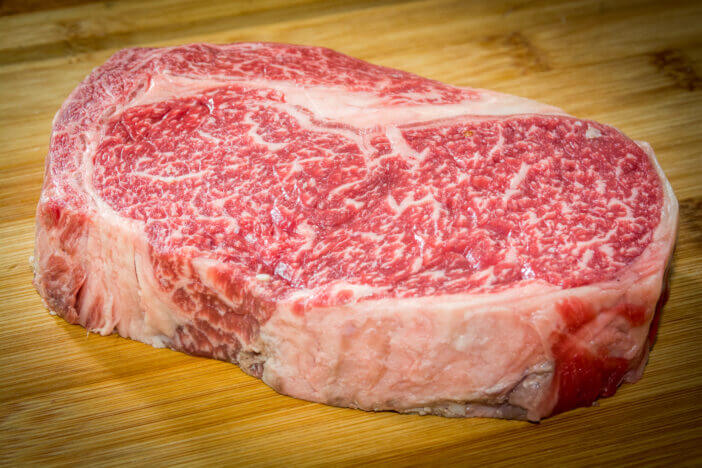 An amazingly well marbled steak is displayed on a wooden cutting board. This thick cut 100% full blooded Wagyu rib eye is a stunner.