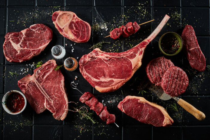 11 Gourmet Meat Gift Sets For This Holiday Season 4 Top view set of steaks consisting of t bone sirloin ribeye tomahawk with skewers and burger patties composed with spatula spices and salt