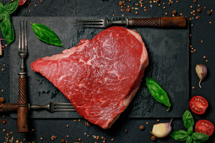 9 Gourmet Meats For Cooking For Home Chefs & Food Bloggers 4 Raw beef steak on a stone cutting board and forks. Grass-fed meat with spices and herbs. Food flat lay