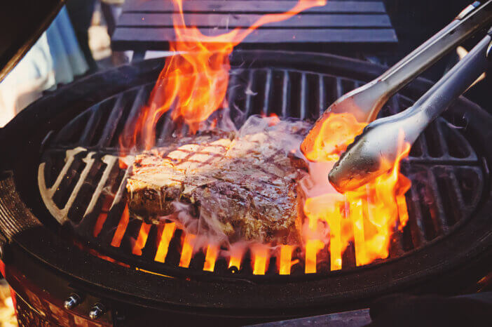 A piece of meat in flame. The cook flips a piece of meat beef on the grill with open fire. Steak on the grill with flames