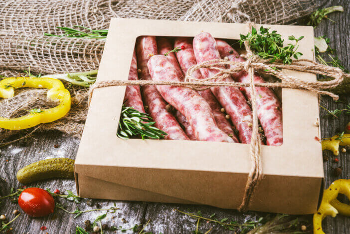 5 Mystery Meat Boxes For Foodies & Culinary Adventurers 3 Raw uncooked meat sausages in a craft box on a rustic cutting board. Spices for raw meat sausages onions, garlic, thyme, rosemary, sage leaves, cilantro, peppers