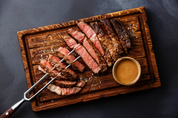 9 Gourmet Meats For Cooking For Home Chefs & Food Bloggers 10 Sliced grilled meat steak Rib eye on meat fork and Pepper sauce on dark background