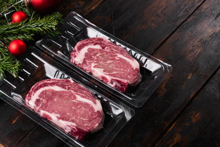 11 Special Occasion Meat Gifts For This Holiday Season 3 Rib eye steak pack with a Christmas tree set, on old dark wooden table background, with copy space for text