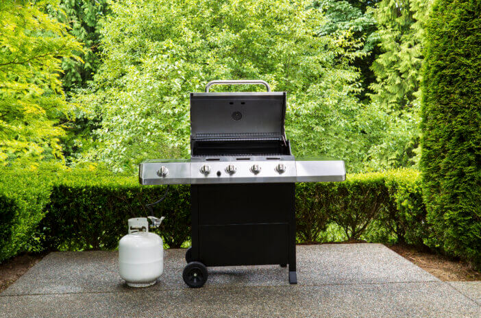 large barbeque cooker, with lid up, on concrete outdoor patio with woods in background