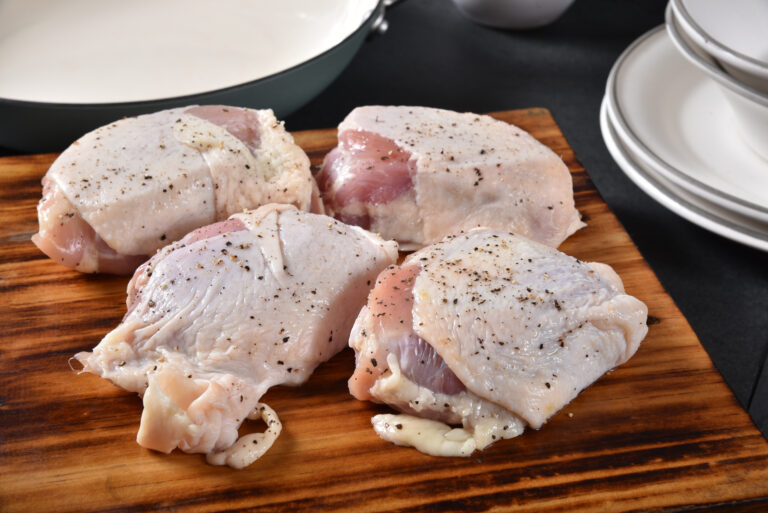 Raw chicken thighs with seasoning on a cutting board near a skillet